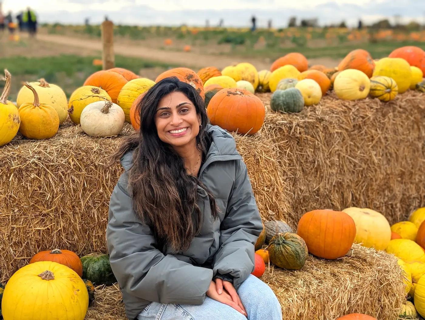 Smiling Dr Patel sitting among colourful pumpkins at a countryside pumpkin patch, celebrating autumn and seasonal energy – The Iron Infusion Centre, Hertfordshire.